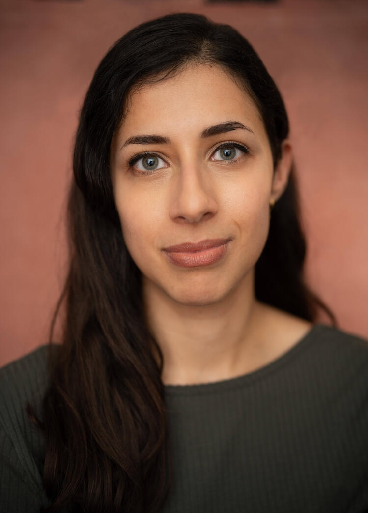 An image of Sarah, a smiling woman with blue-grey eyes and long dark brown hair wearing a green top.